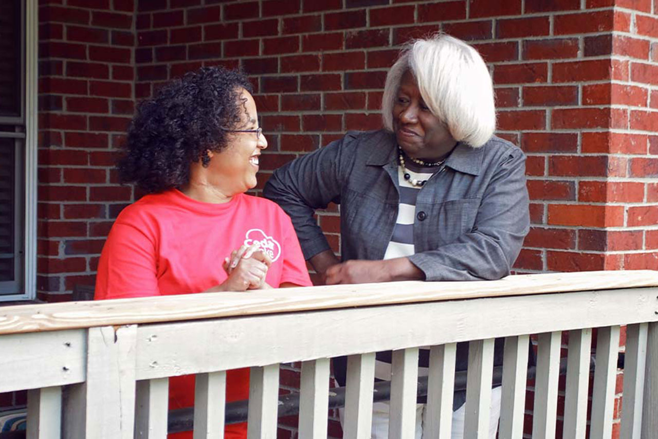 Two ladies look at each other while standing on a porch