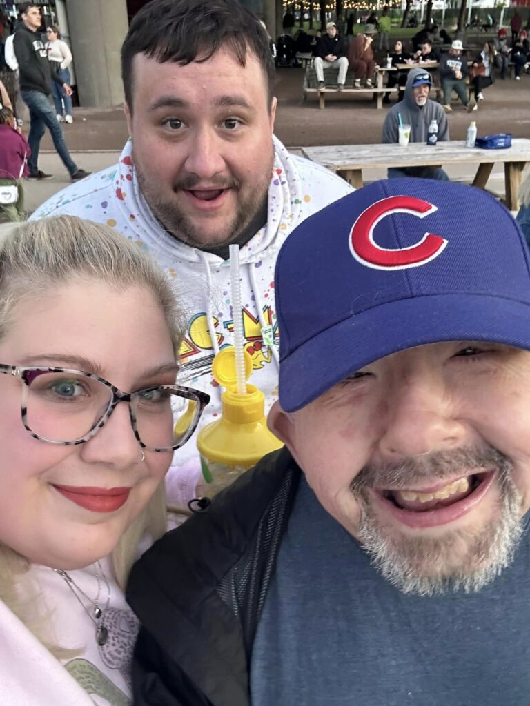Man in Cubs hat smiles with a blonde hair women and man with dark hair and beard