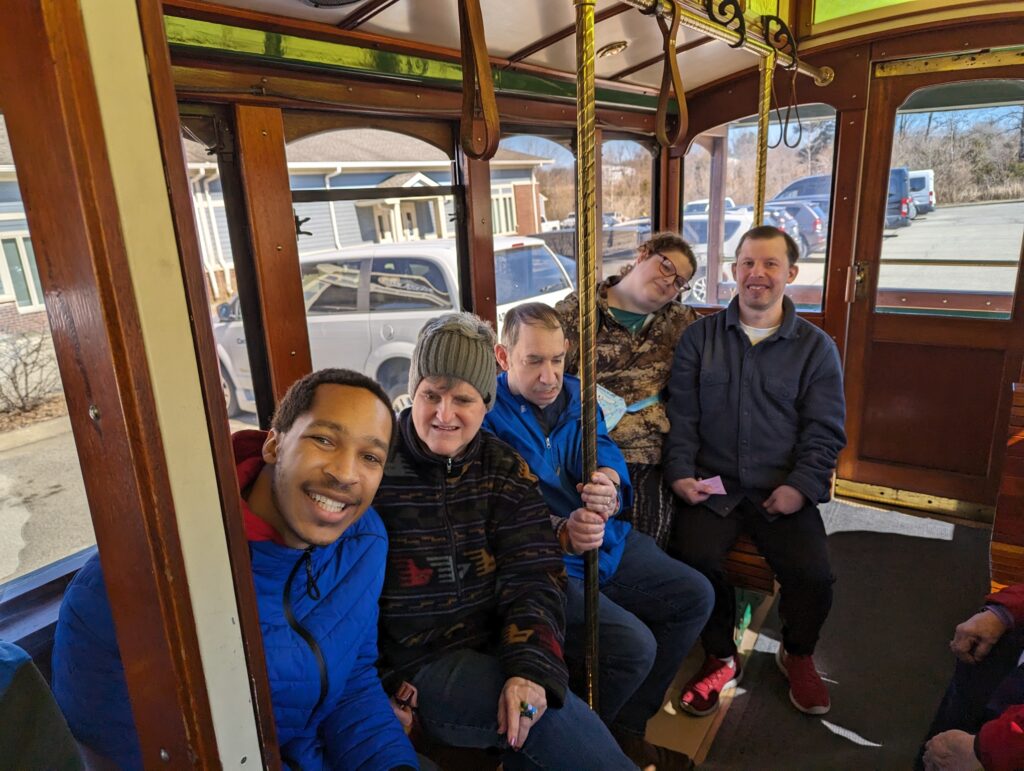 Group of men and women sit on a trolley smiling at the camera