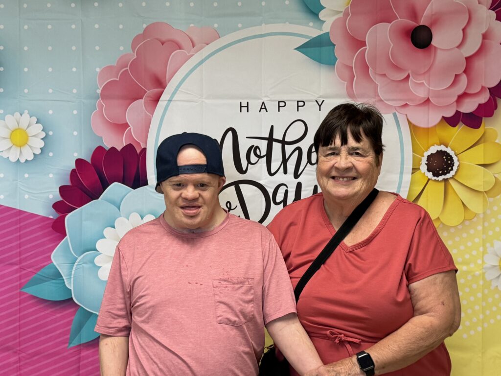 Man with Down Syndrome in pink shirt and black backwards cap stands next to lady in dark pink shirt