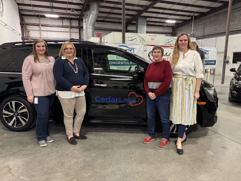 20241220_154717950_iOS Four professional women stand in front of a black minivan