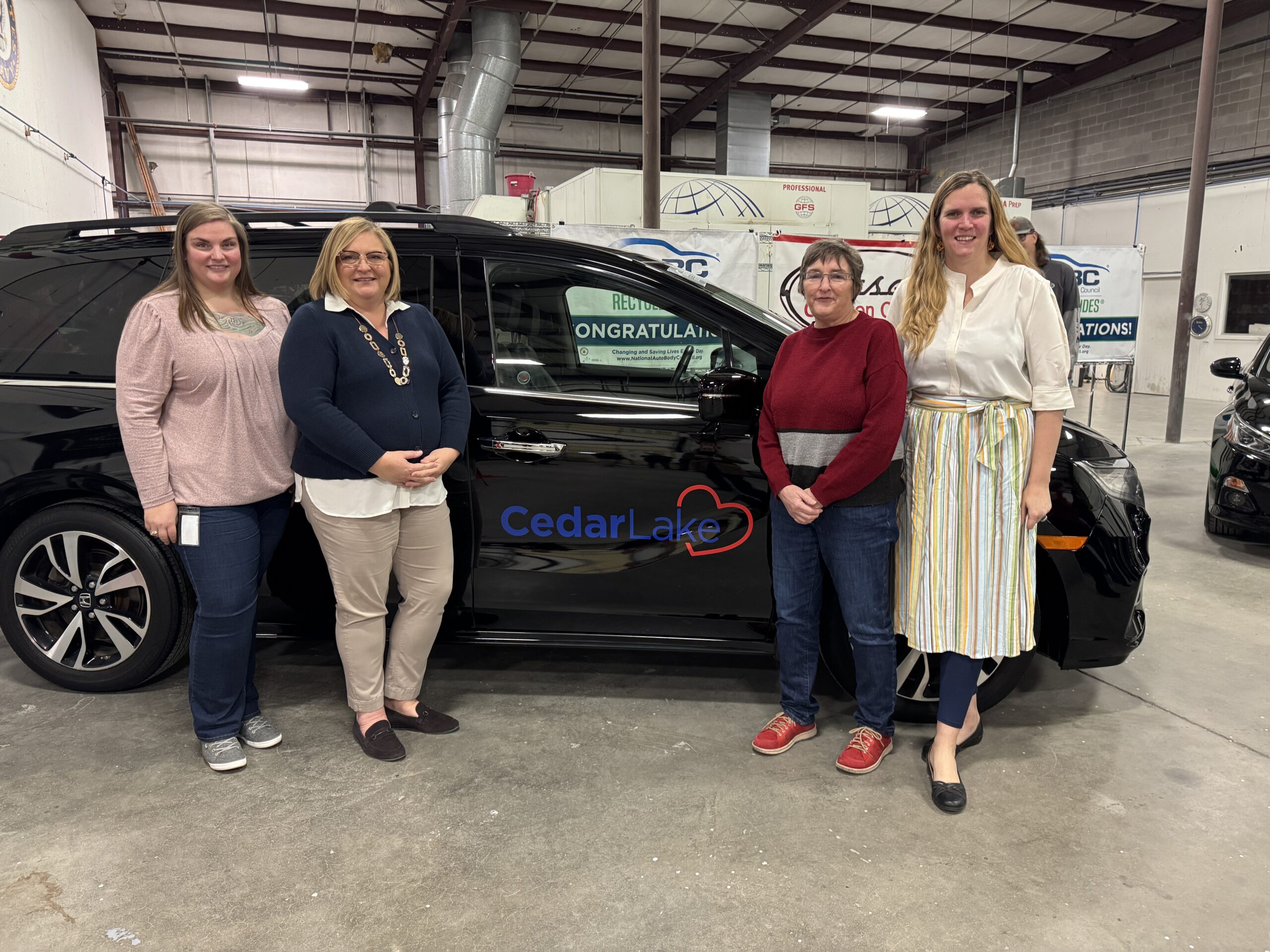 Four professional women stand in front of a black minivan