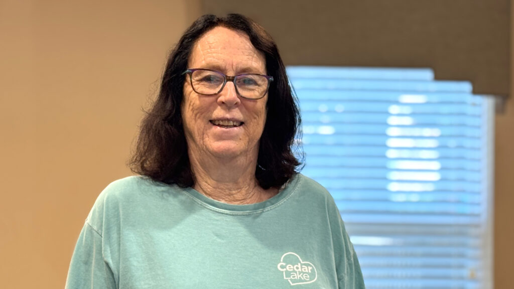 Women stands in front of window wearing a blue Cedar Lake Shirt